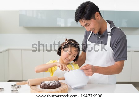 Smiling young man with his daughter preparing dough in the kitchen at home