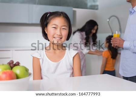 Portrait of a smiling young girl with family in the background at kitchen in home
