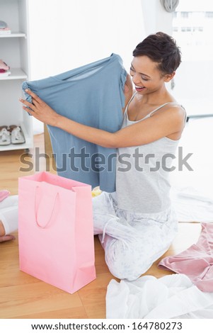 Happy young woman sitting on the floor with new blue t-shirt and shopping bag at home