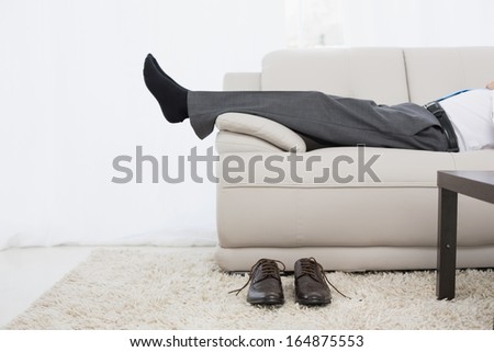 Low section side view of a businessman resting on sofa in the living room at home