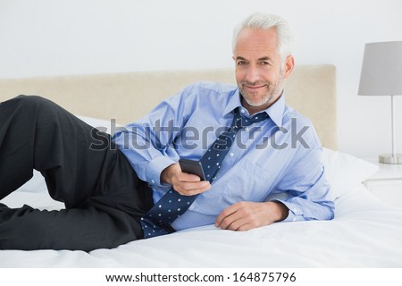 Portrait of a smiling relaxed well dressed man text messaging in bed at home