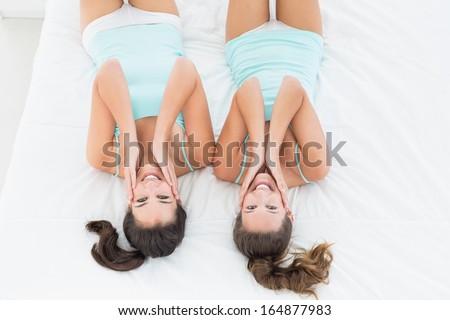 High angle portrait of two young female friends in teal tank tops lying in bed at home