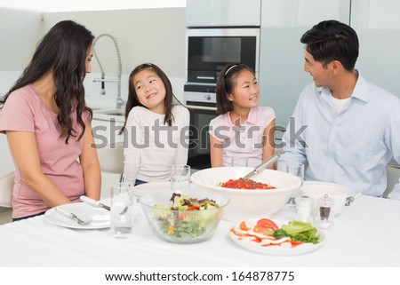 Smiling family of four sitting at dining table in the kitchen at home