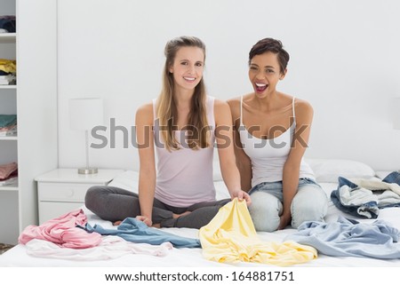 Portrait of two pretty female friends with clothes sitting on bed at home