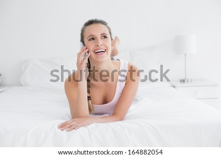 Beautiful smiling young woman using cellphone in bed at home