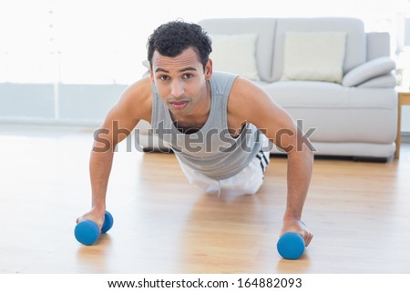 Portrait of a sporty young man with dumbbells doing push ups in the living room at house