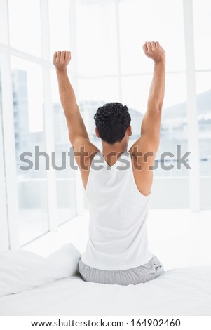 Rear view of a young man waking up in bed and stretching his arms