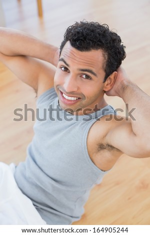 High angle portrait of a smiling young man doing abdominal crunches in the living room at house