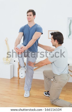 Male therapist assisting young man with stretching exercises in the medical office