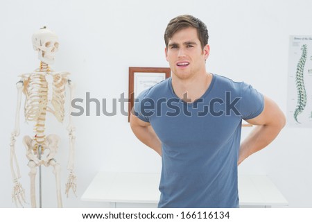Portrait of a handsome young man with back pain standing in the medical office
