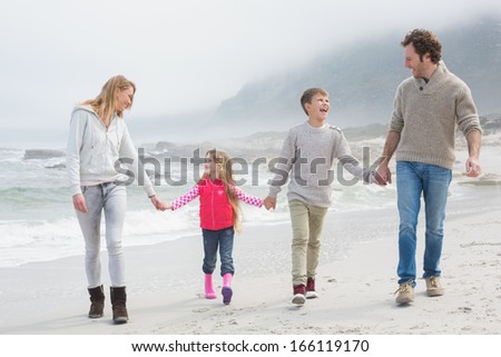 Full length of a happy family of four walking hand in hand at the beach
