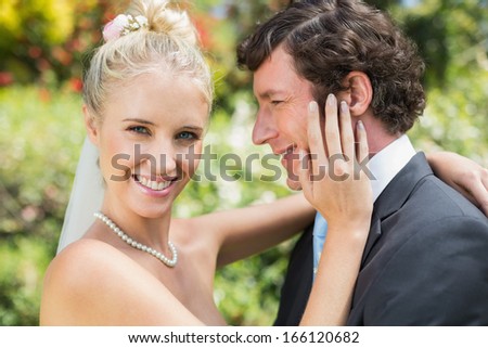 Pretty wife touching her new husbands cheek smiling at camera in the countryside