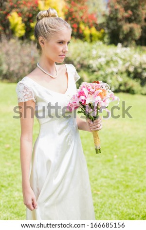 Pretty blonde bride holding lily bouquet in the countryside