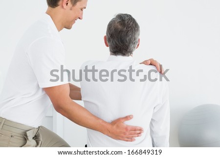 Rear view of a male chiropractor examining mature man at office