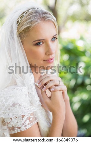 Smiling bride in a veil holding her hands to her chest in the countryside