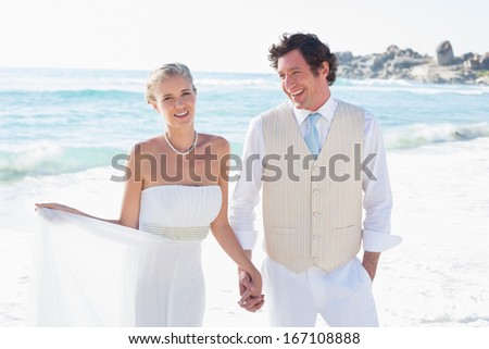 Newlyweds walking hand in hand and smiling at the beach