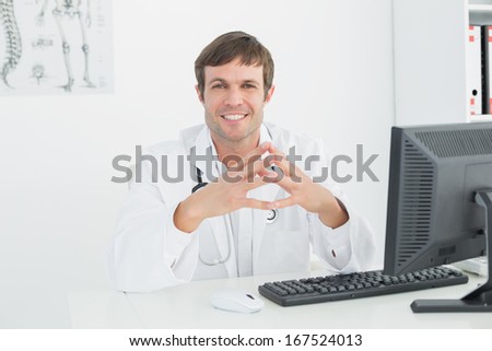 Portrait of a smiling male doctor with computer sitting at the medical office