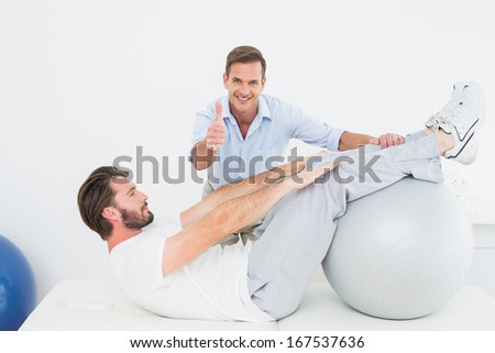 Physical therapist gesturing thumbs up while assisting young man do sit ups in the gym at hospital
