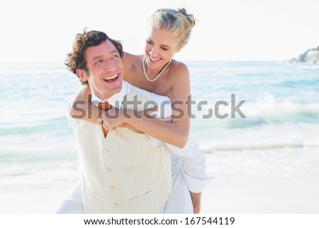 Smiling bride getting a piggy back from new husband at the beach