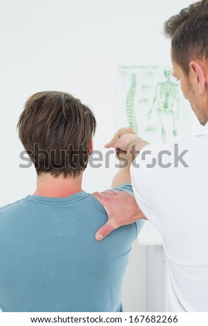 Rear view of a male physiotherapist stretching a young man\'s arm in the medical office