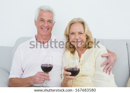 Relaxed senior couple with wine glasses sitting on sofa at home