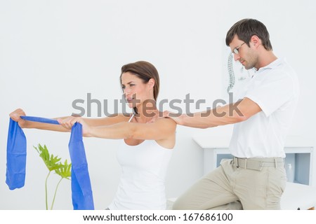 Male therapist assisting young woman with exercises in the medical office