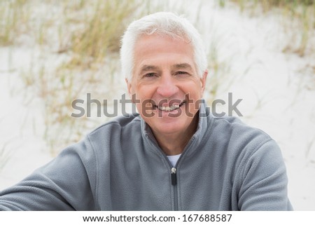 Portrait of a smiling casual senior man relaxing on sand at the beach