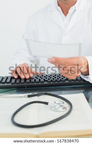 Mid section of a male doctor reading a note at desk in medical office