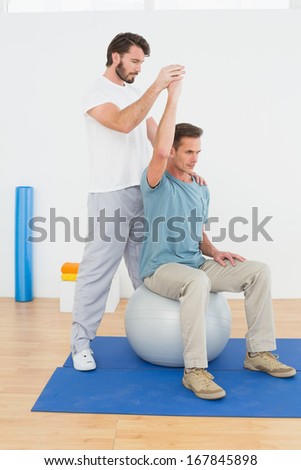 Young man sitting on yoga ball while working with a physical therapist