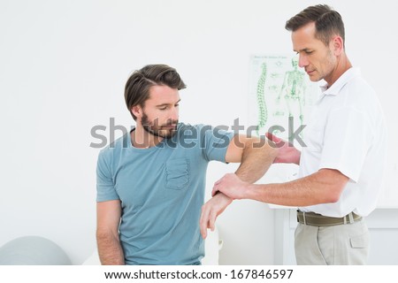 Male physiotherapist examining a young man\'s arm in the medical office