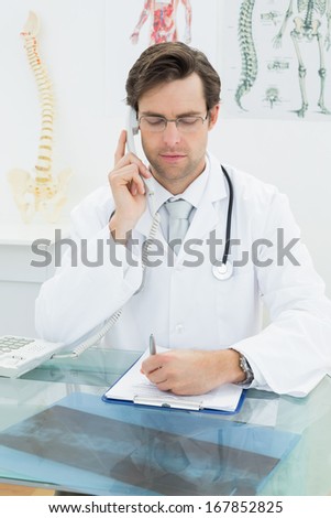 Serious young male doctor using telephone at the medical office