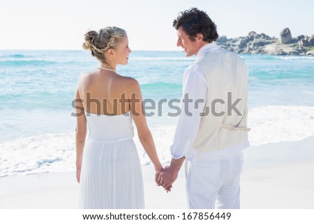 Bride and groom holding hands looking at each other at the beach