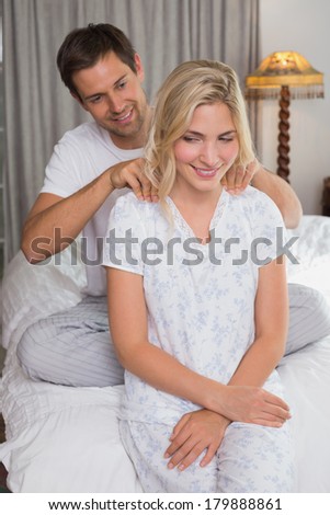 Smiling young man massaging woman\'s shoulders in bed at home