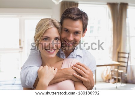 Close-up portrait of a happy young man embracing woman from behind at home