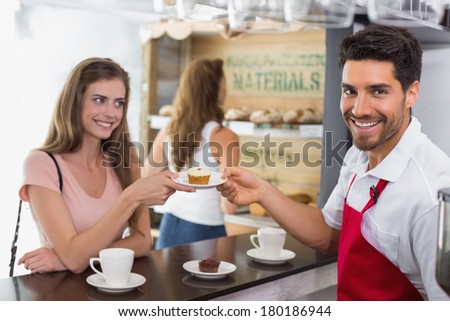 Side view of a male barista giving pastry to woman at counter in the coffee shop