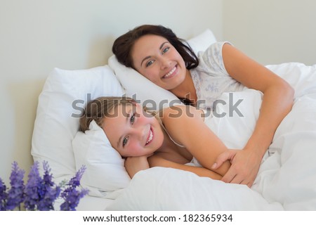 Portrait of beautiful mother and daughter lying in bed at home
