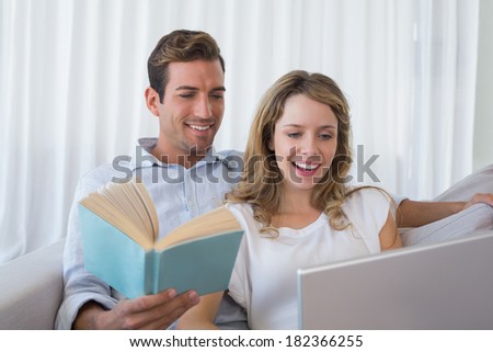 Relaxed loving young couple with book and laptop on couch at home