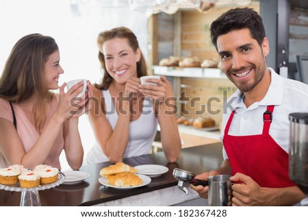 Smiling young women drinking coffee with male barista at counter in the coffee shop