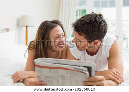 Relaxed young couple reading newspaper in bed at home