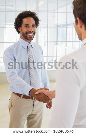 Two smiling young businessmen shaking hands in the office