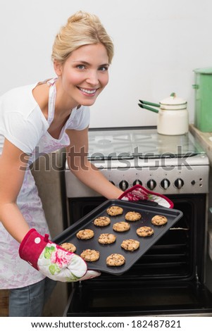 Portrait of a smiling young woman putting a tray of cookies in the oven at kitchen