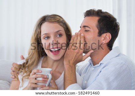 Close-up of a man whispering secret into a cheerful young womans ear at home