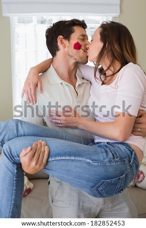 Loving young man carrying woman as he kisses her at home