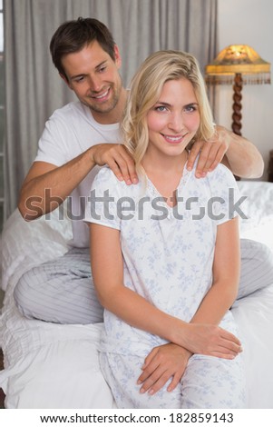 Smiling young man massaging woman\'s shoulders in bed at home