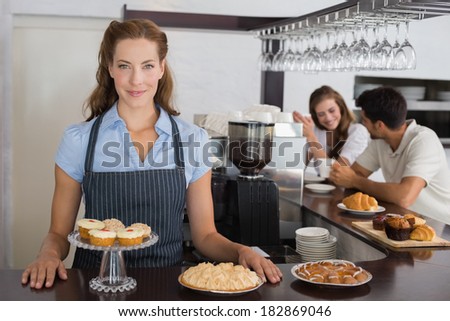 Portrait of a smiling female cafe owner with sweet snacks and couple at counter in the coffee shop