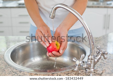 Close-up mid section of hands washing apple at washbasin in the kitchen