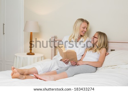Mother and daughter looking at each other while reading story book in bed