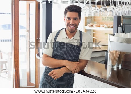 Portrait of a smiling confident young waiter standing at the cafe counter