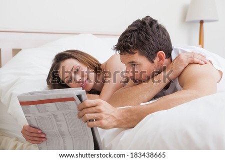 Relaxed young couple reading newspaper together in bed at home