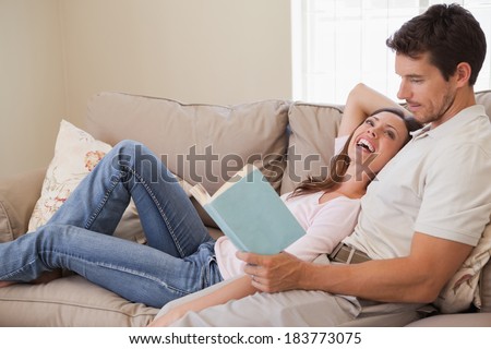 Side view of a relaxed young couple reading book on couch at home